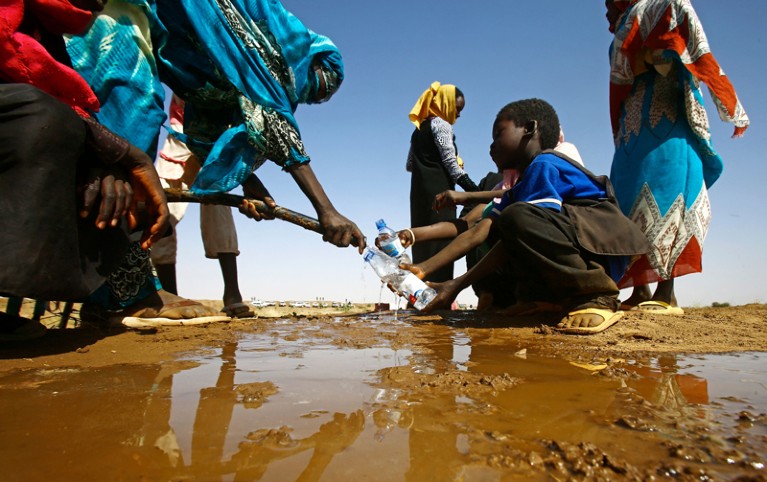 A low-angle view of a Sudanese woman filling a young boy's water bottle